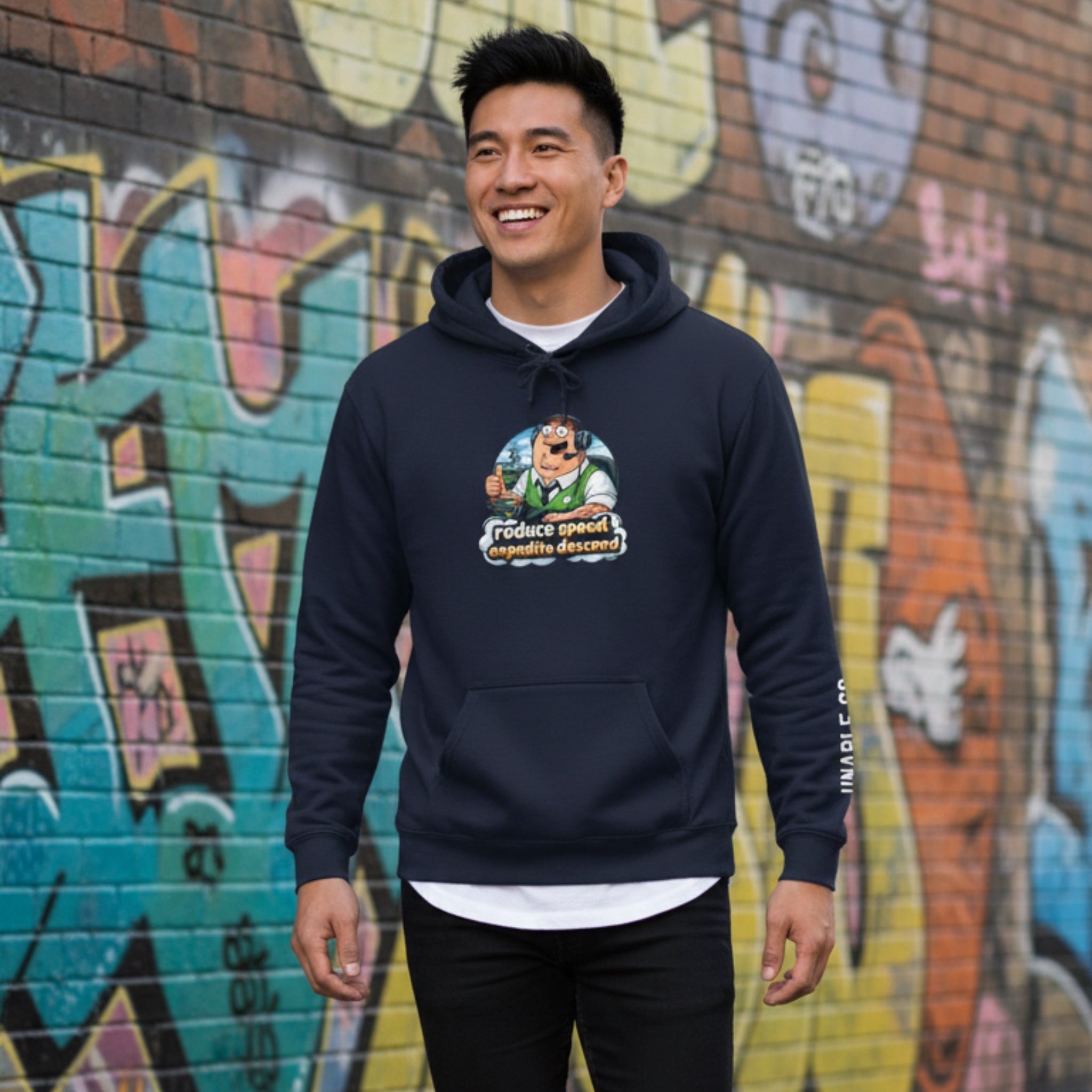Man wearing a navy hoodie with a graphic design in front of a graffiti-covered wall.